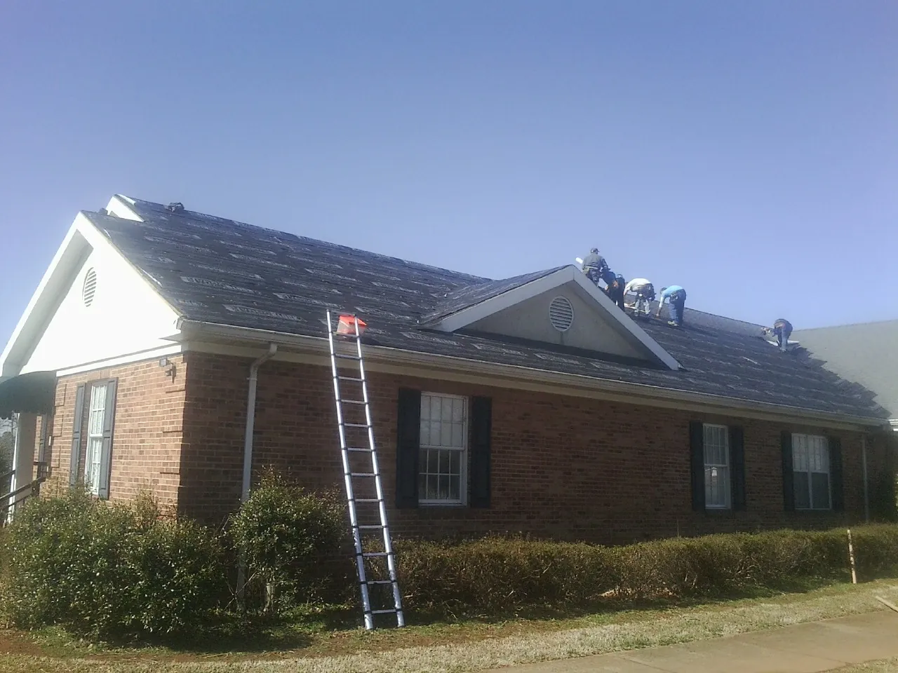 Crew tearing shingles off a brick ranch roof with a ladder set — Emergency Roof Repair work by our crew in Westfield